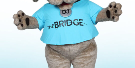 Dog Mascot with DJ headset, sunglasses, and blue t-shirt with The Bridge Logo